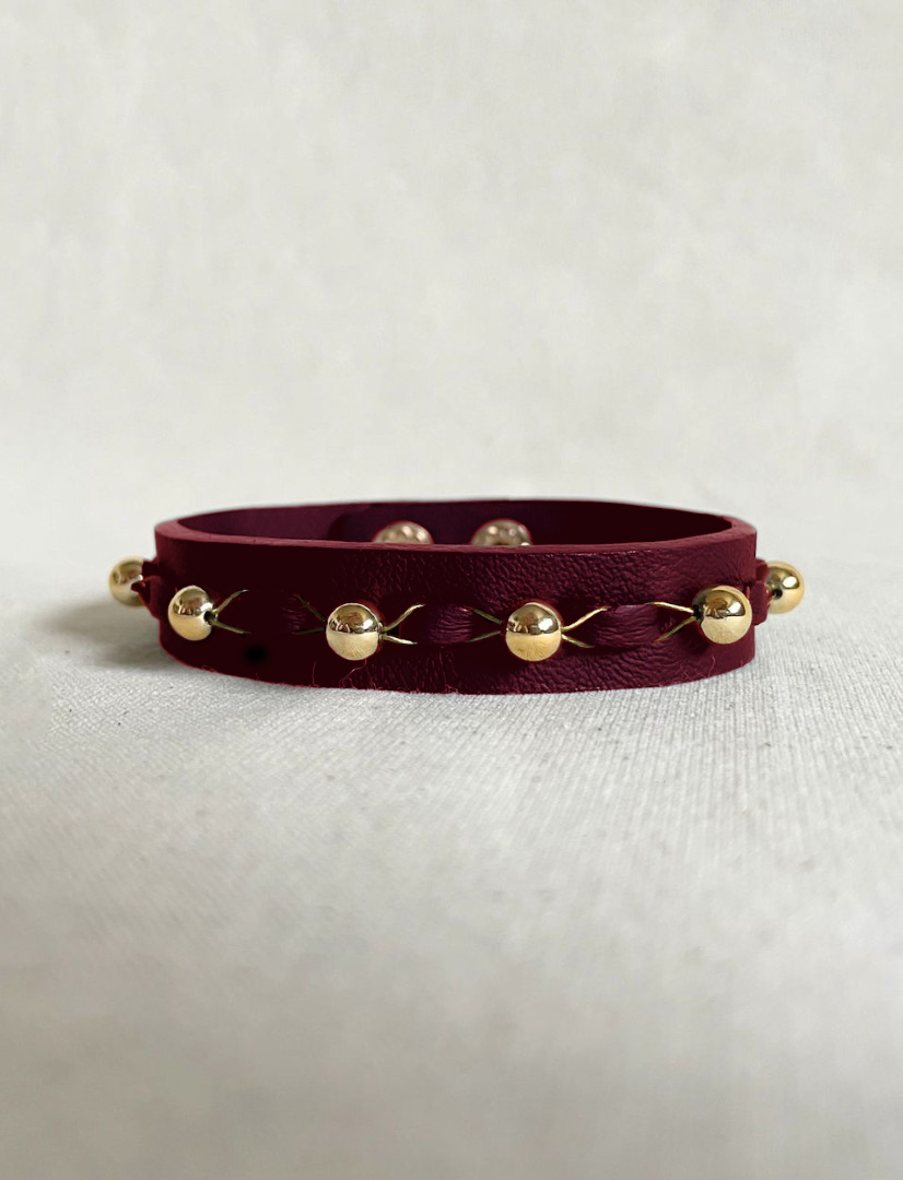 Timeless burgundy leather bracelet with upcycled gold beads and handcrafted stitching on neutral fabric