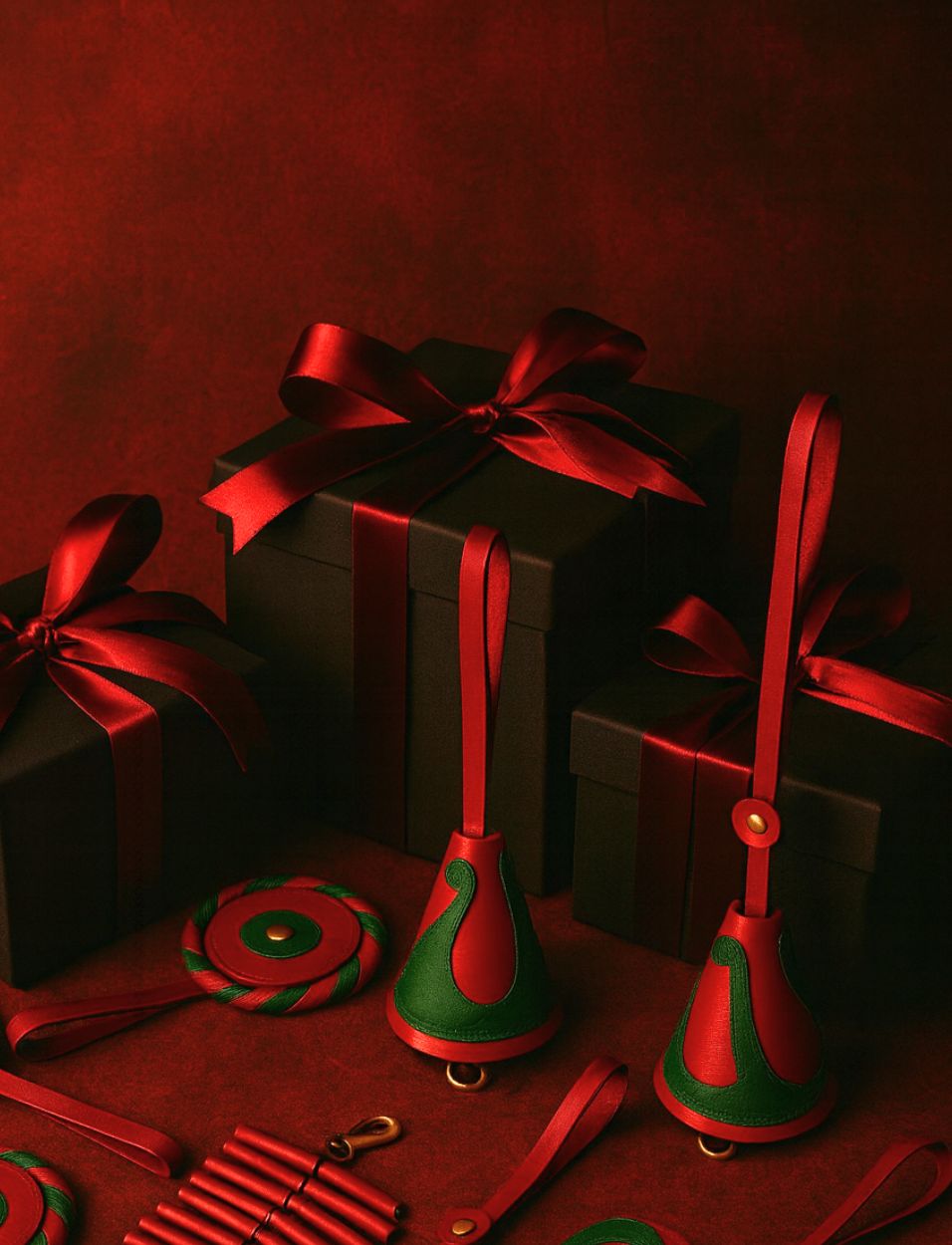 Black gift boxes wrapped with red satin ribbons surrounded by red and green leather Christmas ornaments