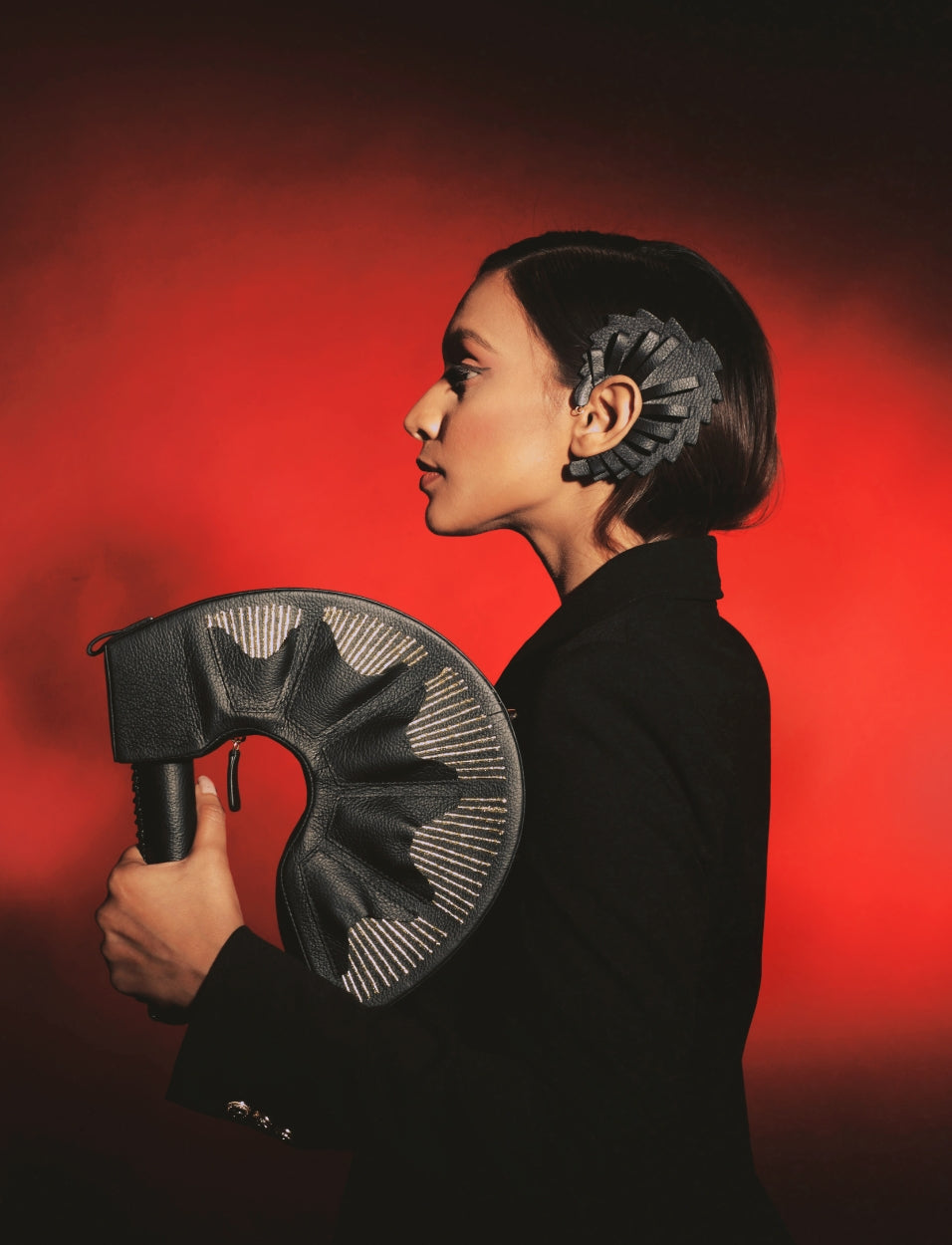 Profile of woman in black holding black leather curved bag, black headpiece, red background