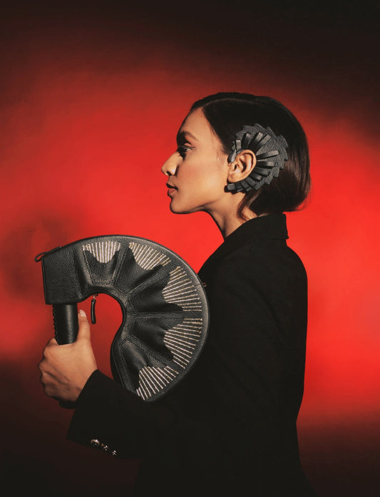 Profile of woman in black holding black leather curved bag, black headpiece, red background