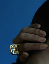 Hand wearing a large gold geometric metal ring against a solid blue background