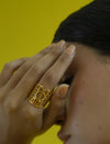 Close-up of hand with a gold geometric metal ring on finger against yellow background