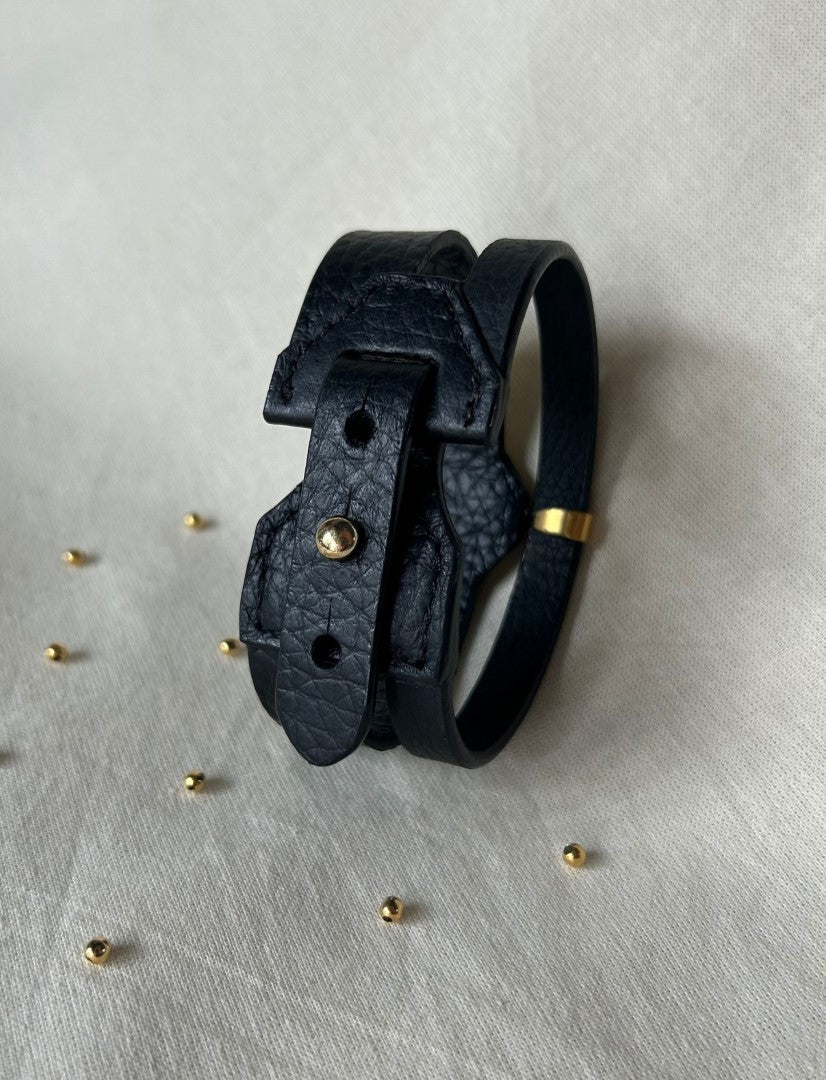 Handcrafted black leather upcycled bracelet with gold accent on beige fabric, small gold beads scattered