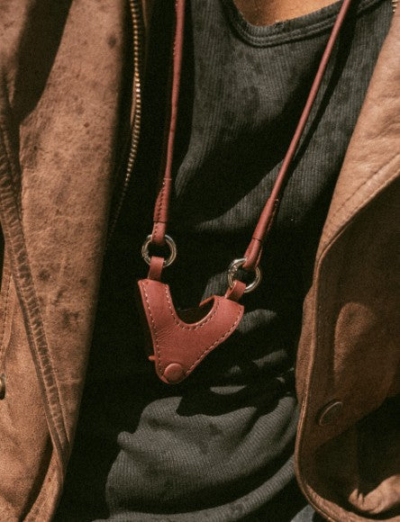 Brown leather camera strap worn over black shirt and brown jacket with zipper and button details