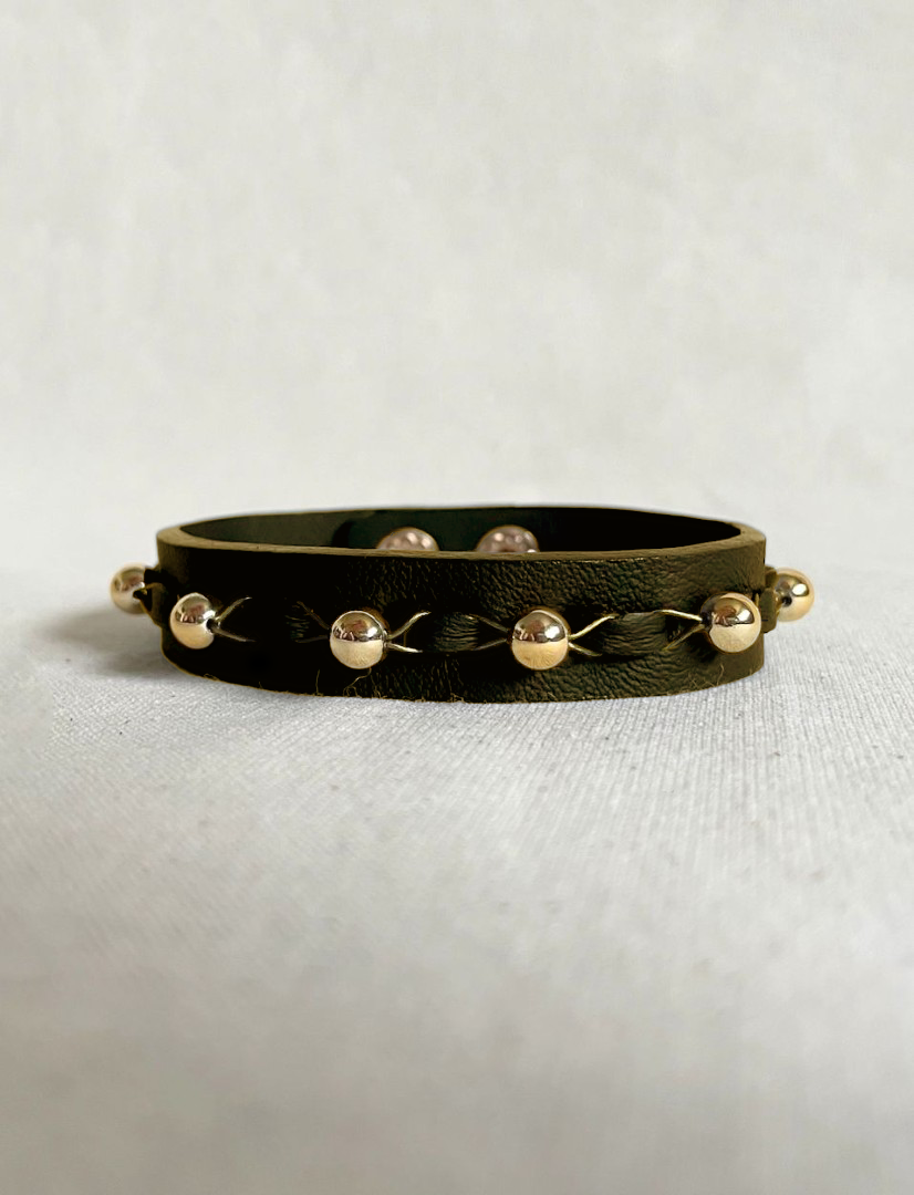 Black olive leather unisex bracelet with upcycled gold-tone beads and braided design on white fabric