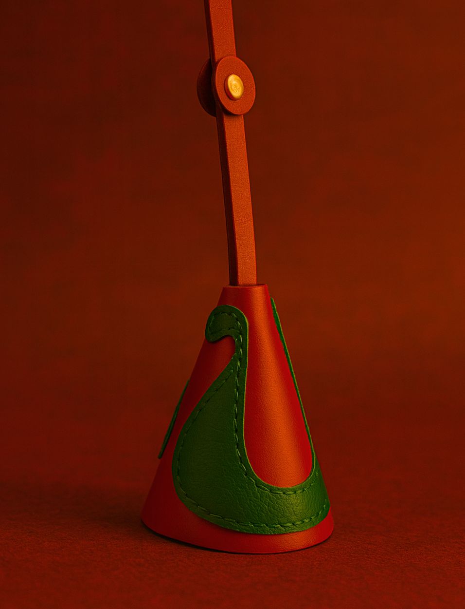 Red and green leather bag charm with gold button on red background