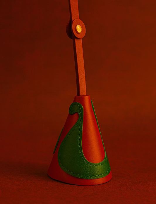 Red and green leather bag charm with gold button on red background
