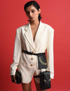 Model wearing oversized white blazer with gold buttons and black leather belt bags against red background