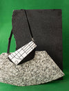 Black and white geometric patterned handbag with black strap on textured stone slabs against green background