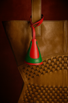 Brown leather bag with woven detail and red and green leather bell-shaped charm