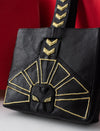 Black leather tote bag with gold geometric embroidery and bold strap design against red background