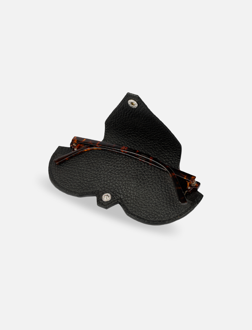 Black textured leather eyeglass case open with folded tortoiseshell eyeglasses inside on white background