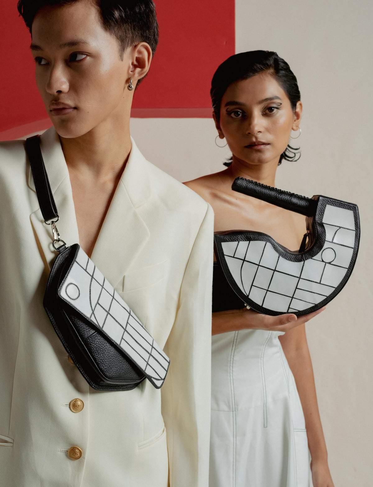 Two models showcasing black and white geometric handbags with leather details against abstract red and beige backdrop