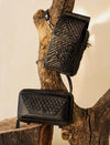 Two black textured leather crossbody bags displayed on natural wooden branches