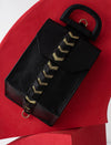 Black textured leather handbag with gold chevron strap on curved red surface