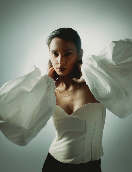 Woman wearing white corset top with large puffed sleeves and geometric gold necklace