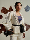 Woman wearing cream pantsuit with black striped sleeves, patterned navy top, black belt bag, and matching clutch
