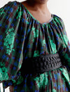 Close-up of person wearing green and blue floral plaid blouse with puff sleeves and black woven belt