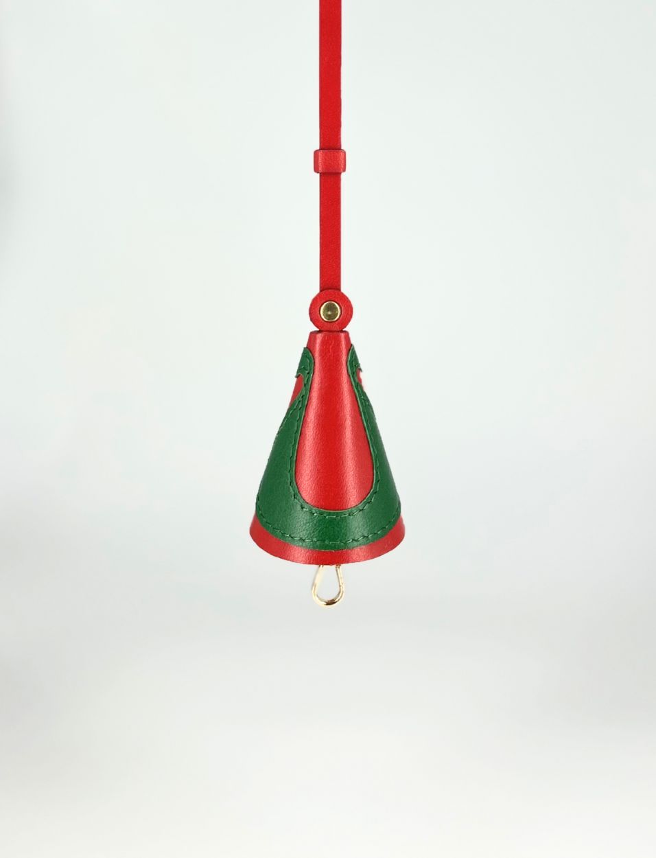 Red and green leather handbag charm with gold hardware hanging against white background