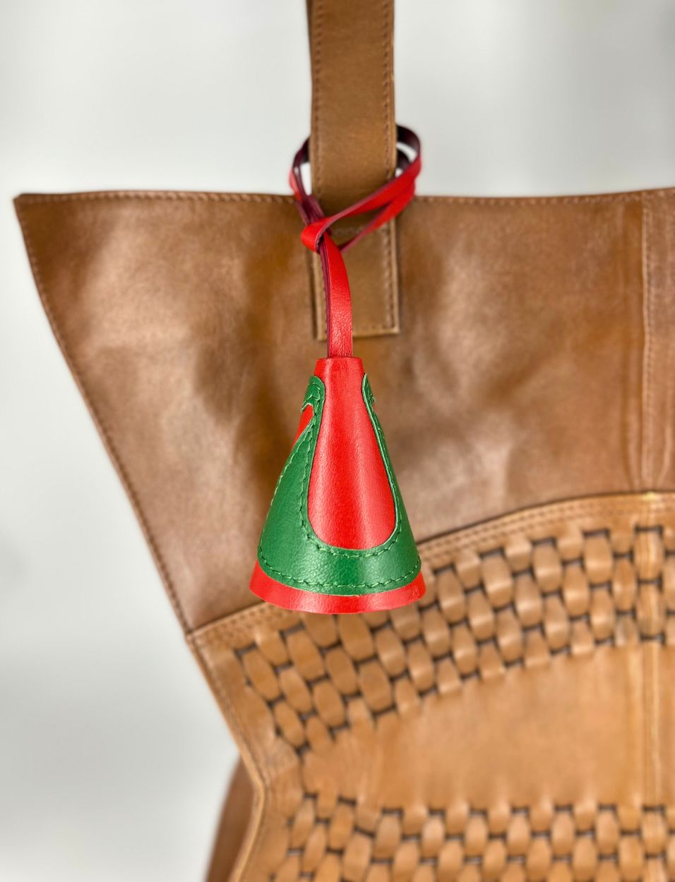 Red and green leather charm attached to brown woven leather handbag strap