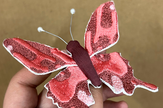 Red butterfly sticker held by a hand against a brown background