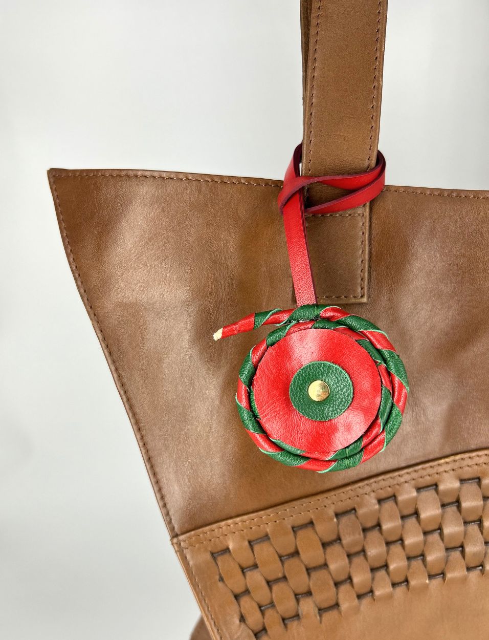 Brown leather tote bag with woven detail and red-green braided leather charm attached