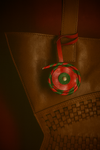 Brown leather bag with woven detail and a red and green braided leather keychain charm