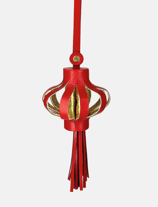 Red and gold hanging lantern charm ornament with tassels on white background