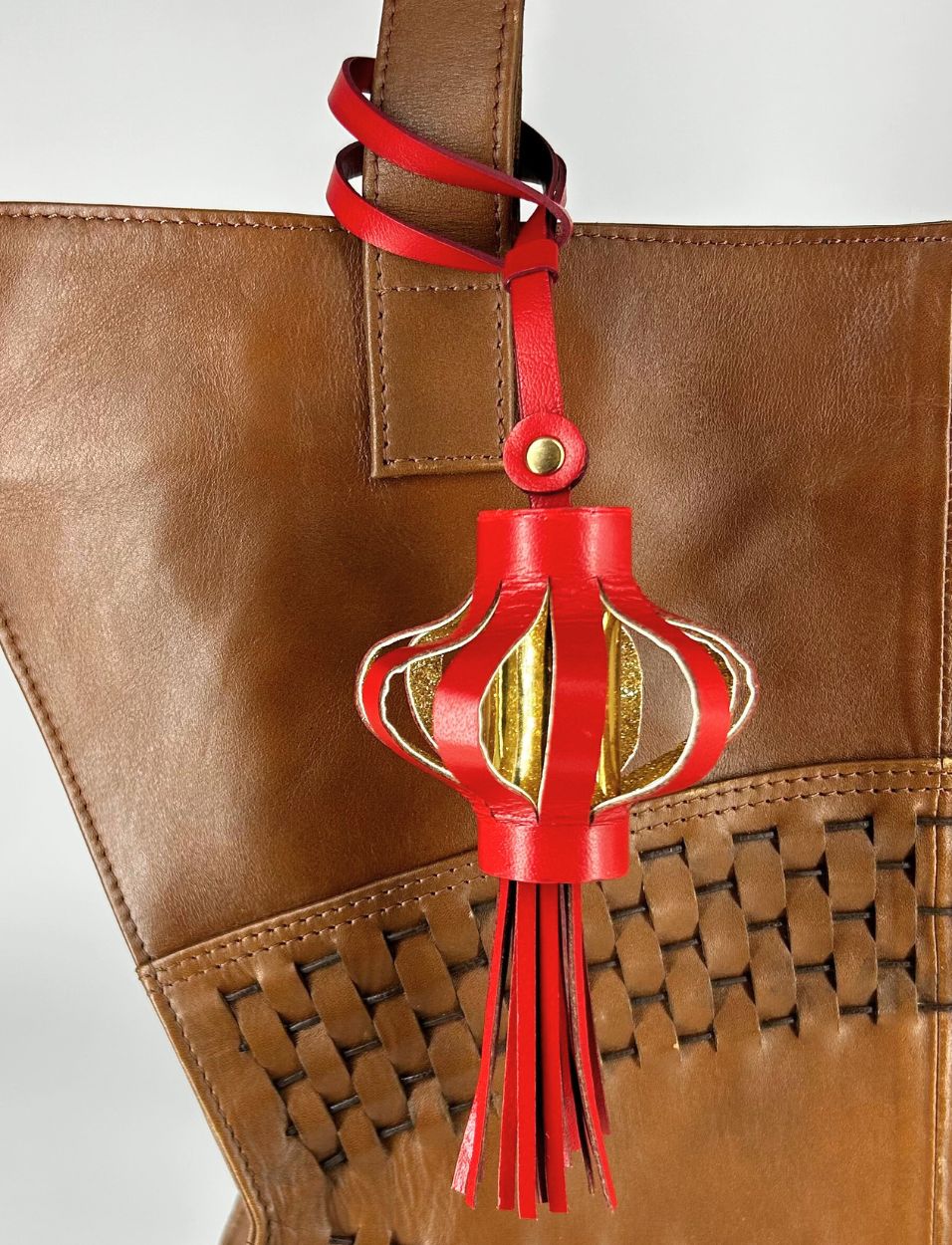 Red leather lantern charm with gold accents hanging on brown woven leather bag