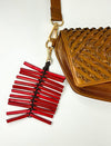 Brown woven leather handbag with attached red leather tassel keychain on white background