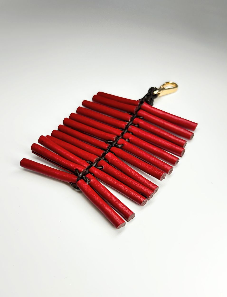 Red wooden stick keychain with black braided cord and gold clasp on white background