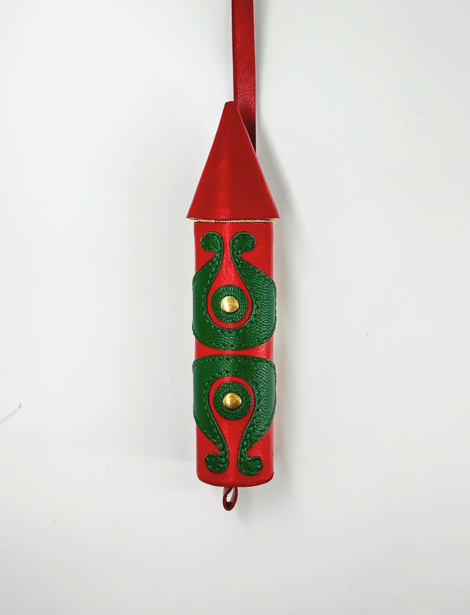 Red rocket-shaped leather charm with green embossed decorative patterns and gold studs on white background