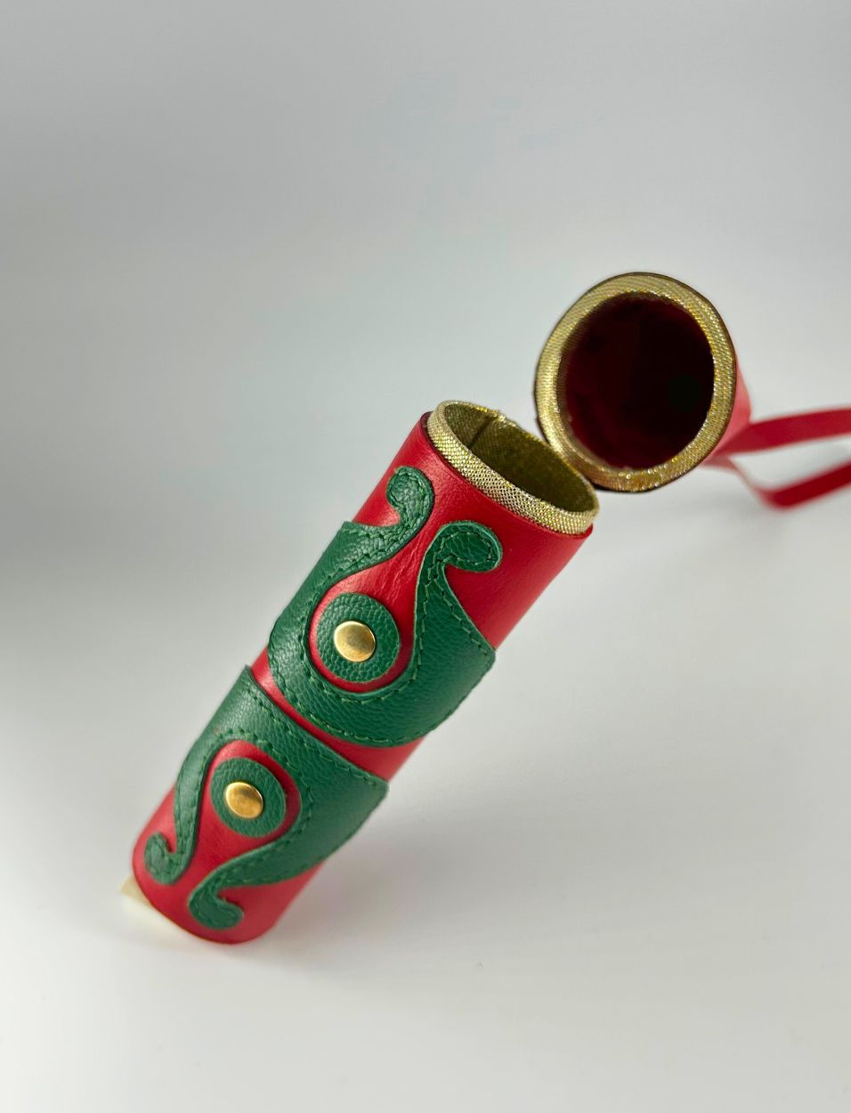 Red and green leather cylindrical case with gold button details and a gold-rimmed open lid