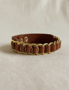 Brown leather bracelet with gold chain links on beige fabric background
