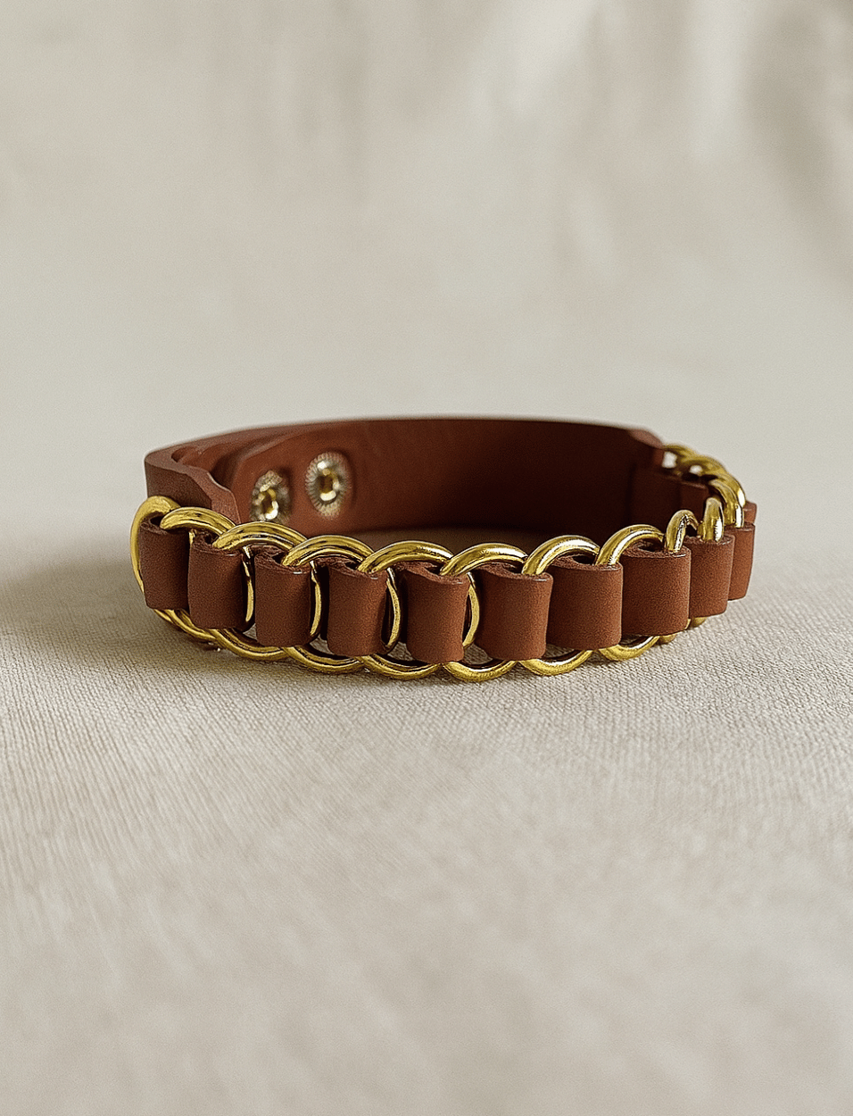 Brown leather bracelet with gold chain links on beige fabric background