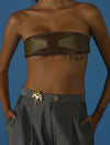 Close-up of woman wearing brown leather bandeau top with gold accents and gray pants with gold lion brooch